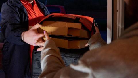 Hands passing two flat cardboard boxes to another person at a doorway