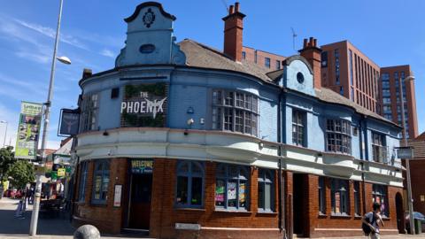 The Phoenix is a two-storey building on the corner of Gosford Street and Whitefriars Street in Coventry city centre. The lower level is red brick with a white band separating the upper and lower floors. The upper floor is painted in Coventry Blue and has bowed windows.