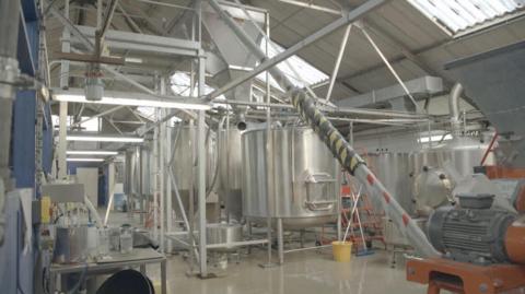 Inside the brewery. There are many stainless steel vats and pipes in a sterile-looking room.