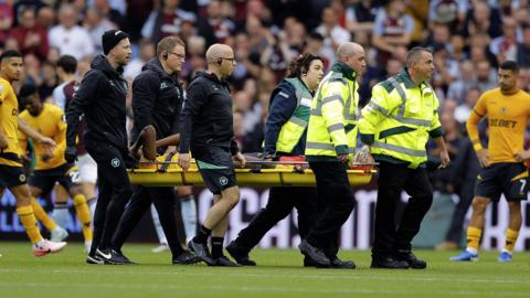 Yerson Mosquera, who has his hands to his face, is carried off by three paramedics and three members of Wolves' medical staff at Villa Park. 