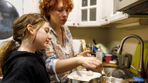 A mother and daughter cook food together in a kitchen