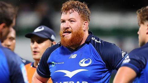 Harry Johnson-Holmes in blue Western Force shirt, looking slightly to left of frame with team-mates either side in foreground