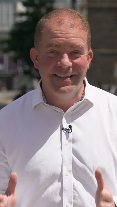A man in a white shirt, with short hair is looking at the camera