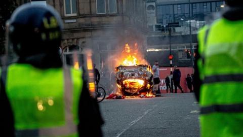 Taken from behind two police in riot gear, a car burns