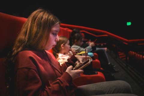Teenager sitting the cinema looking at her phone 