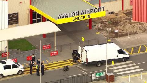 The entrance of Avalon airport with a white van and police officers standing in front of it