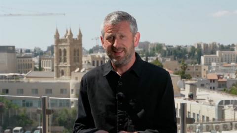 Jon Donnison in a black shirt in front of Jerusalem skyline.