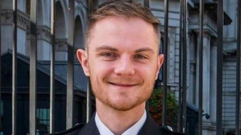 Former Norfolk Police sergeant Marley Jay Symonds wearing his formal police attire. He has short brown hair, ginger stubble and is smiling