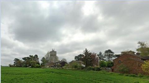 Green fields with trees at the boundary and a water tower