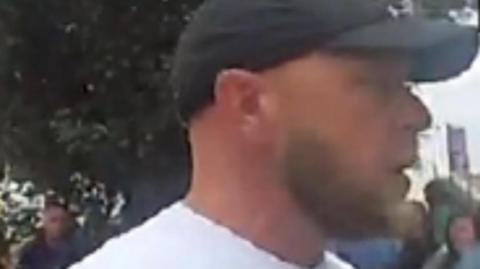 A man wearing a baseball cap and a white t-shirt in a crowd