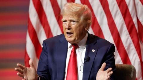 Donald Trump sitting in front of American flags