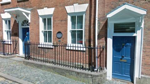 Numbers 9 and 10 on Priory Row in Coventry. The properties have blue doors, white frames and black railings. In front of the two houses are cobbled pavements. 