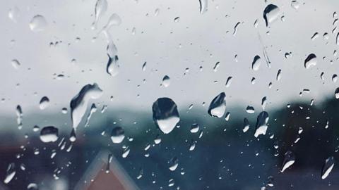 Raindrops on window that overlooks a house on a street