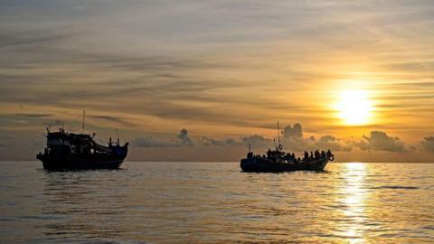 A boat carrying Rohingya refugees (left) sails ashore off the coast of Labuhan Haji in Southern Aceh province in 2024