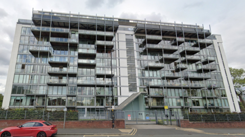 A wide shot of the front of Warwickgate House, which is a grey colour and covered in windows, and each apartment has a balcony