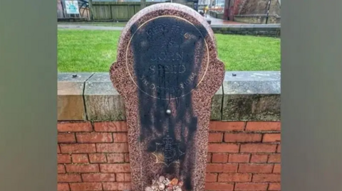 A memorial stone defaced with black paint.