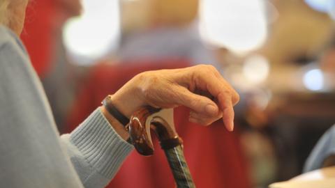 A stock image showing the hand of an elderly person perched on a walking stick. 