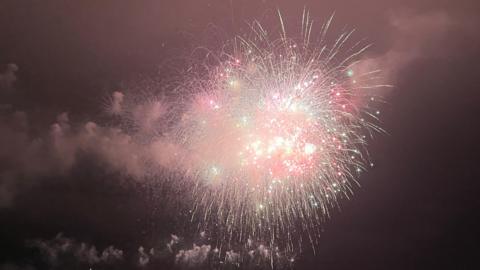 A firework lights up the night sky. Smoke is in the sky around the firework.