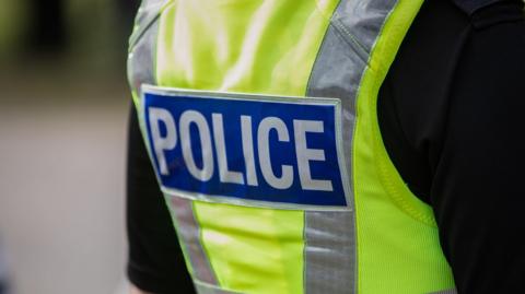 A closeup of a police officer wearing a black t shit and a high vis police vest