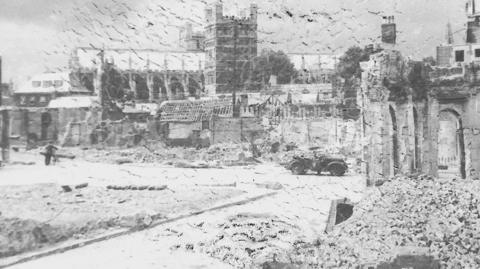 A damaged archive photo taken by Henry Wykes shows Exeter Cathedral surrounded by the remains of buildings badly damaged in a German bombing raid. There is a huge pile of rubble in the foreground and the top of the photo shows clear signs of chemical deterioration which is destroying the negative.

