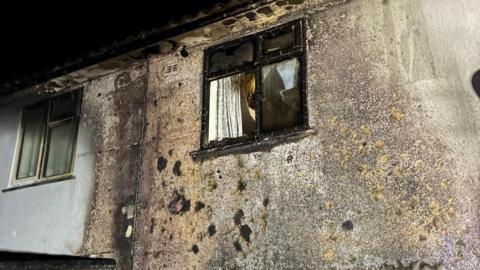 A picture of rendered houses with a window that's been shattered and blackened by fire. Smoke damage is apparent on the walls of the terraced properties.