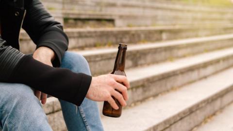 A person holding a bottle of alcohol on some steps.