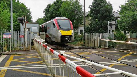 A train is crossing a railway line which has red and white barriers across the road. There are markings on the road.