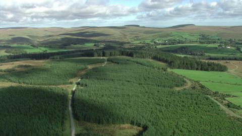 An aerial shot of some fields, hills and grasslands. Cloudy skies.