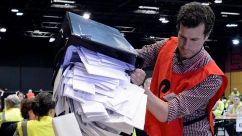 Man pores a box of votes onto a table 