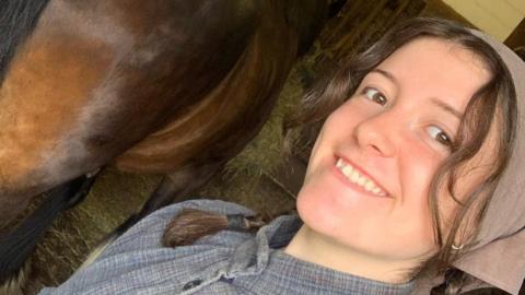 Alys Harrison next to a horse. She is taking a selfie and smiling. She has a head bandana on. 