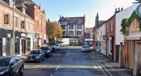 Image is a Google Street View shot of Henry Street in Lytham. There are cars parked along the side of the road, in front of various bars and shops. 