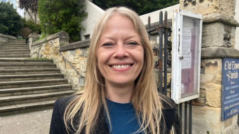 Sian Berry smiles at the camera, in the background there are some steps and a wall