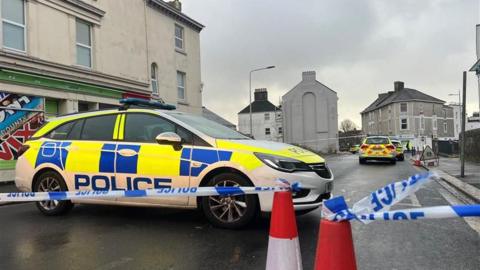 A number of police cars behind a blue and white police cordon on West Hoe Road in Plymouth. 