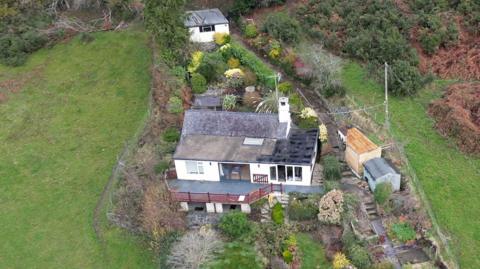 Aerial view of Daniel San Diego's house, a white villa with a balcony offering striking views of rolling hills and a well-manicured garden