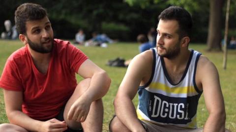 Two bearded men dressed casually sit next to each other in a park