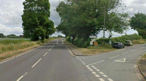A country road with signs at the junction of a minor road.
