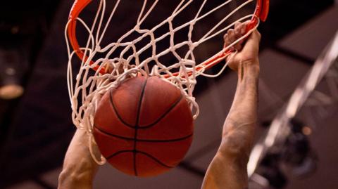 Male basketball player dunks the ball with two hands. Close up on the rim, net and ball.