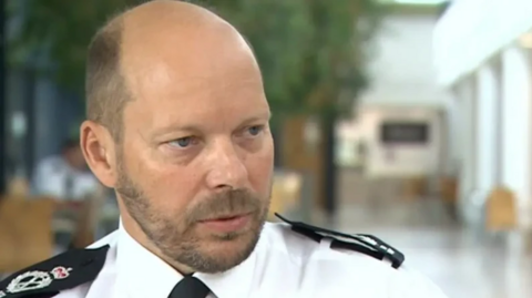 Head and shoulders shot of Rod Hansen wearing police uniform looking to the right. He is partly bald, with dark, short hair and a closely shaved beard.