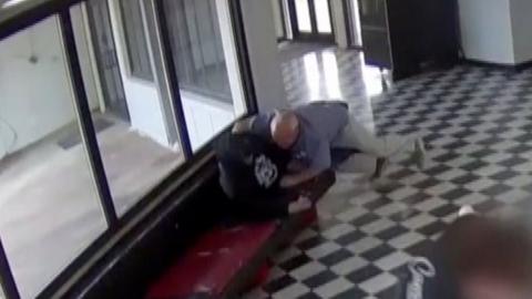 A still from CCTV footage showing a male in light coloured clothing lunging towards another male in dark clothing.