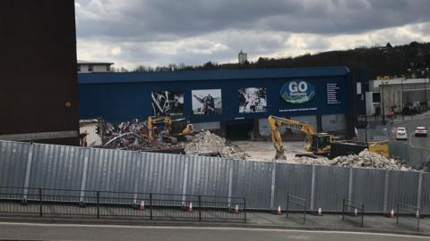 Demolition of a former retail site. There is rubble and two diggers.