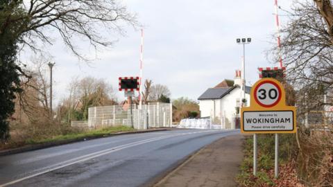 A general view image of Easthampstead Road level crossing, with a sign to the right which says: "Welcome to Wokingham, please drive carefully".