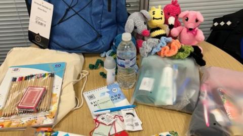 A table with essential items including dental kits, snacks and colouring packs and a blue grab bag.