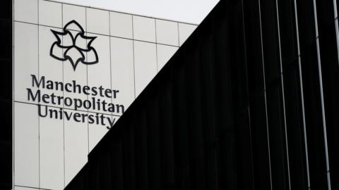 Exterior shot of a metal-covered building with the Manchester Metropolitan University name and logo on it.