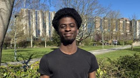 A man stands outside under a tree on a sunny day. 
