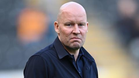 Henrik Pedersen, wearing a black jacket, looks straight-faced while on the touchline during Sheffield Wednesday's game at Hull City on 21 March