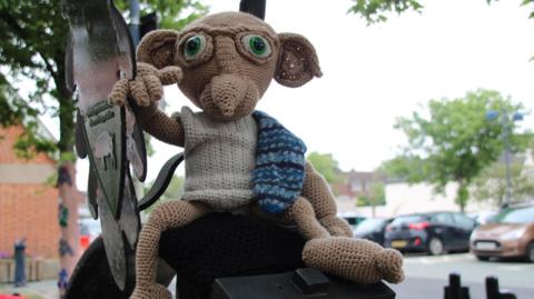 A knitted version of Dobby perched on a postbox