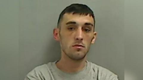 A mugshot of Liam Matthews who has short dark hair and wears a grey T-shirt.