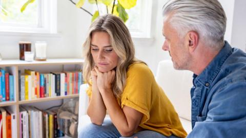 Woman sits on sofa and man sat on her right looks at her