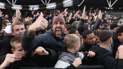 Bromley fans celebrate beating York City at Hayes Lane to reach the National League promotion final at Wembley, with one fan giving a thumbs-up gesture to the camera