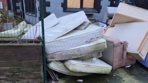 A pile of old mattresses and a dirty pink sofa outside former pub The Spellow. The mattresses are covered in brown and green stains.
